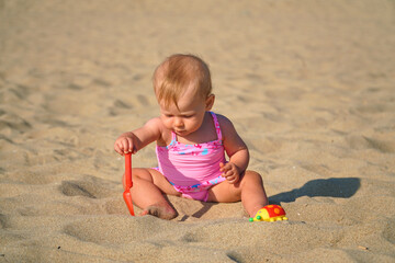 Happy baby in the sand plays. Cheerful little kid playing on the beach on a sunny day. High quality photo