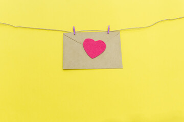 paper envelope with a pink heart hanging on colored clothespins on a yellow background. valentine day concept. color of the year 2021