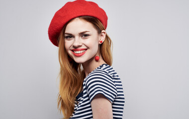 Cheerful woman in red hat and striped T-shirt gesturing with hands and smiling 