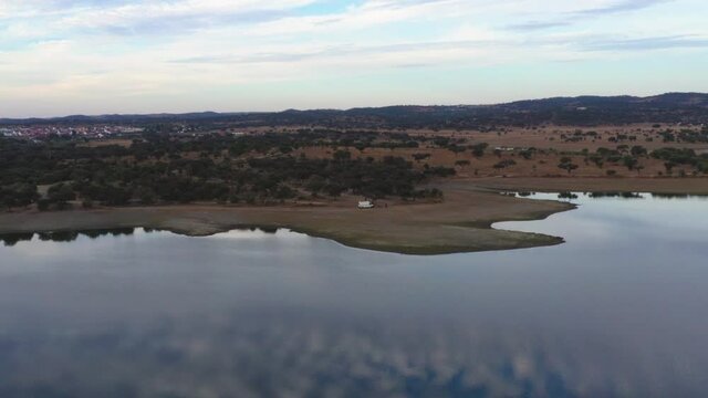 Drone aerial view of Camper van on an Alentejo dam lake landscape and under the shade of olive and cork trees, in Portugal