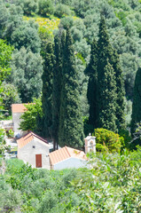 View of small white houses with a chapel, framed by dark green cypress trees. Valley in the plateaus of the Greek island of Crete. Hot but humid climate.