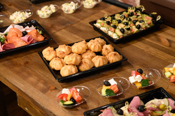 food in disposable food packaging. Vegetable salads, meat, sweets in black plastic dishes at a party