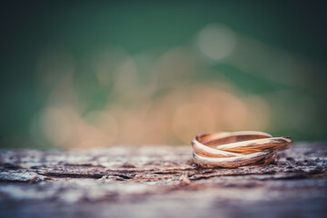 Close-up of a ring with three rings on wooden table with green background. Wedding jewelry in gold, white gold and rose gold. macro shot with selective focus and copy space for text