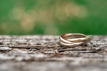 Obraz na płótnie Canvas Close-up of a ring with three rings on wooden table with green background. Wedding jewelry in gold, white gold and rose gold. macro shot with selective focus and copy space for text