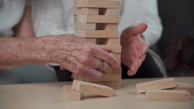 Senior woman practice skills build wooden blocks, building tower and trying not to let it fall, Jenga game. Old patient pull out block, place on top, support dotor during therapy dementia in house.