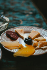 Close up. White plate with different types of cheese, salami and figs cut into thin slices on the dining table. Traditional Italian appetizer in Palermo, Sicily, Italy. European cuisine