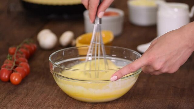 Whisking fresh raw chicken eggs in a glass bowl.