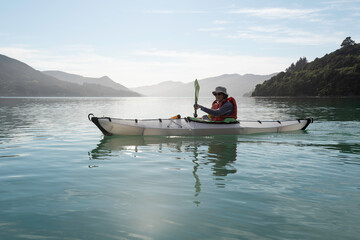 A kayaker on Kenepuru Sound on a calm morning looking into the sun. Marlborough Sounds, New Zealand.