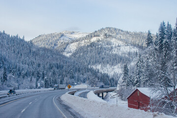 Snow-covered highway among the mountains, on the sides there are trees and trees in the snow. Winter landscape with snow-covered road, fir trees and mountains in Montana, America, 1-18-2020