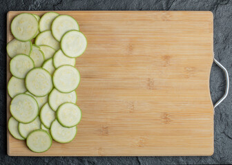 Zucchini and slices in wooden board on black background