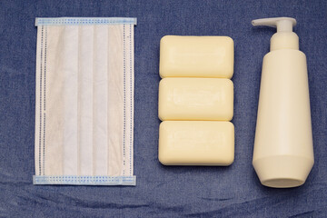 flat lay with hand sanitizer gel in spray bottle and antibacterial soap, medical mask on denim background