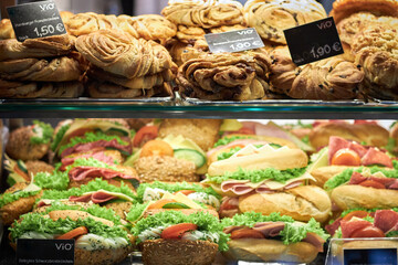 Sandwiches and pastries are stuffed for sale in a shop window. Display window of a bakery and pastry shop of a European city with puff bakery and sandwiches, close up