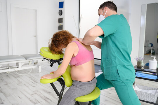 Shot of young physiotherapist massaging back of pregnant woman. Man wearing protective face mask during new normal. High quality photo