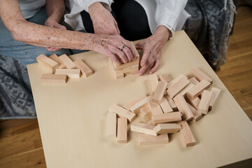 Fototapeta na wymiar Mature doctor conducting session, therapy for senior patient in nursing home, training fine motor skills for dementia, alzheimer disease and recovery institute by folding wooden blocks, playing jenga