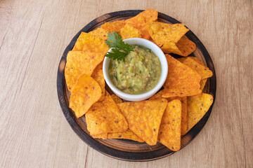 White bowl with guacamole sauce and some corn nachos on a wooden board. 45 degree view