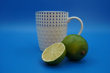 White with a blue pattern cup of tea, a lime and a half of a lime. Close-up, blue background.