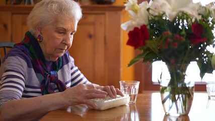 Low angle of elderly woman taking pills out of weekly organizer, putting it into her mouth and drinking water.