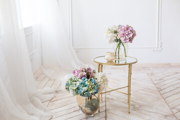Fototapeta na wymiar Tender simple interior in light colors with tule, bouquets of artificial hydrangea and elegant mirror table on light parquet floor
