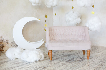 Elegant soft sofa near a concrete wall. Luxury interior of child room in white colors. Decorative moon in a room. Armchair with fabric upholstery