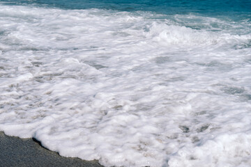 White foamy waves on sandy beach closeup. Seaside on sunny summer day. Summer vacation time concept.