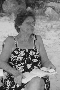 foto em preto e branco de uma senhora ledo um livro na praia