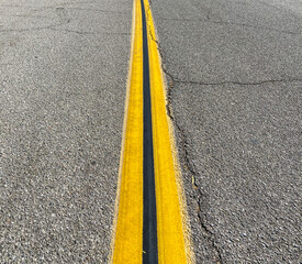 cracked asphalt road with bright yellow center stripe down the middle with black line