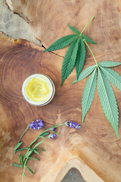 Still life detail of CBD massage lotion and cannabis leaves on a piece of rustic wood