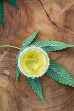Still Life Detail Of CBD Massage Lotion And Cannabis Leaves On A Piece Of Rustic Wood