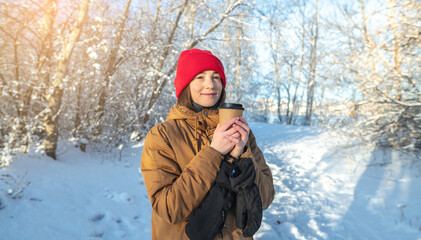 Young woman is drinking hot coffee on a frosty winter Sunny day outdoors in the forest