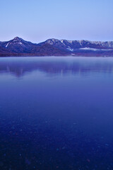 冬山と静水の湖面。夜明けの湖の風景。