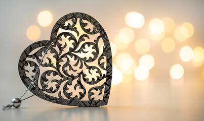 Fototapeta premium Carved wooden heart on a grey background with a golden bokeh