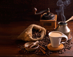 cup of coffee and coffee beans in a sack on dark background, top view