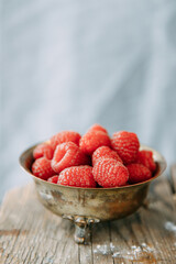 A pile of raspberries in a metal plate with a blurry background. Ripe raspberries close-up on a wooden table.