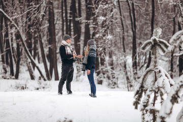Fototapeta na wymiar Kneeling guy puts an engagement ring on a girl's hand, making a proposal to get married in winter in a snowy forest