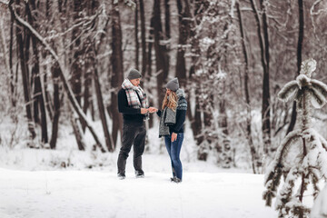 Fototapeta na wymiar Kneeling guy puts an engagement ring on a girl's hand, making a proposal to get married in winter in a snowy forest