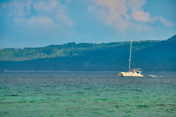 Obraz premium Philippines, Boracay island, Puka Beach. A white yacht is moored in the sea with a white rubber boat attached. Against the background of the mountain and palm trees of the neighboring island.