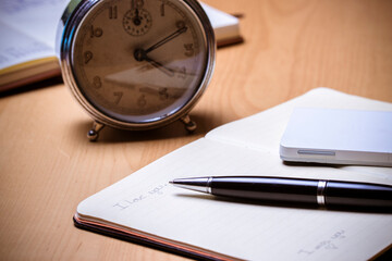 Note book with an alarm clock in the background.