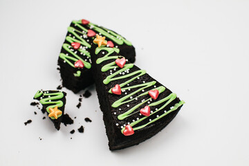 Slice of Fresh Homemade Chocolate Brownie with green icing and festive sprinkles close up. Sweet homemade Christmas or winter holidays pastry food concept.
