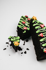Slice of Fresh Homemade Chocolate Brownie with green icing and festive sprinkles close up. Sweet homemade Christmas or winter holidays pastry food concept.