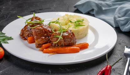 stewed beef pieces in sauce with mashed potatoes and carrots on a white plate. The hot dish is beef stew.