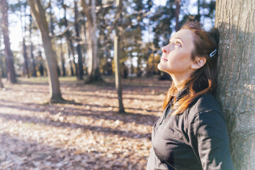 beautiful woman leaning on tree trunk in the forest thinking and enjoying the good weather.