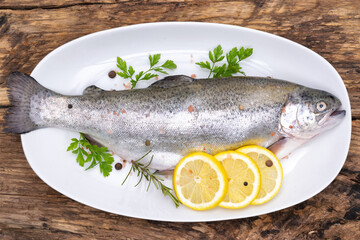 Top view of a raw rainbow trout marinated in fresh herbs and lemon ready for cooking on a plate in rustic style