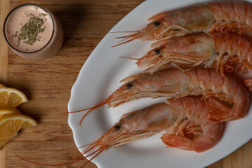 Flat lay image of unpeeled king prawns served with lemon slices and cocktail sauce as a starter or...