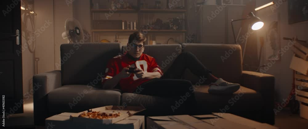 Wall mural POV Portrait of Caucasian teenager playing video game inside home garage, enjoying pizza. Shot with 2x anamorphic lens