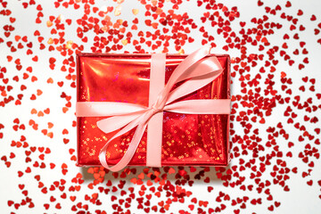 Flat lay of bright red present with pink ribbon bow with lots of small glitter hearts