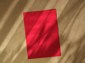 Empty red rectangle poster mockup with soft shadow on golden beige wall background. Flat lay, top view