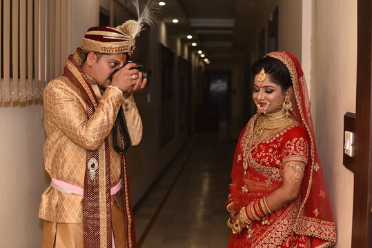 Young Indian wedding couple posing for photographs. Groom clicking picture of bride. The couple is  wearing traditional wedding dress which is designer lehenga and sherwani