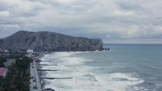 Shooting drone flight over amazing nature sea with coastline beach surf wave swell. Aerial view beautiful cliff formation with city Sudak infrastructure surrounded by seascape and cloudy sky. Part 2