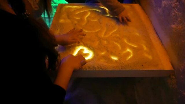 Little girls in the salt room play with salt and draw patterns on a luminous table during Halotherapy. Close-up hands