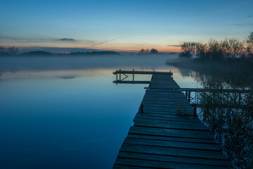 Fototapeta na wymiar Footbridge on the lake and evening fog